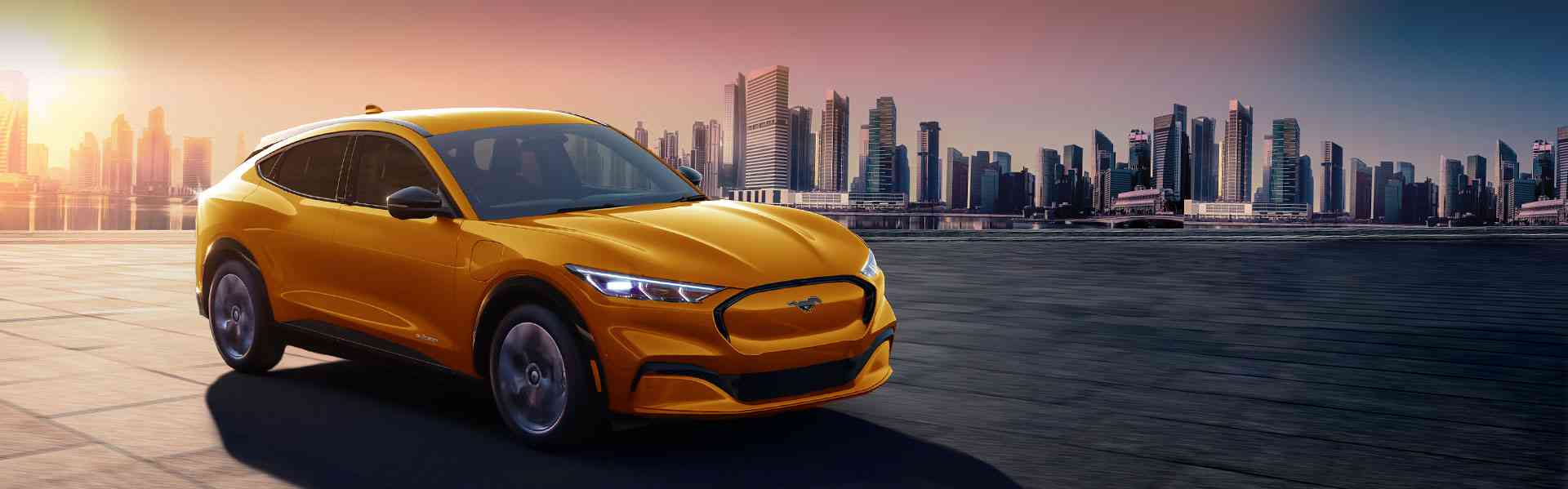 New 2023 Ford Mustang Mach-E in vibrant yellow against a city skyline at sunset, featured in Chinook Auto Sales inventory.