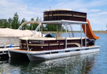 Canalake Double Decker pontoon boat with a water slide, docked on a lake surrounded by trees.