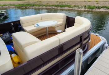 Canalake Double Decker boat seating area with cream-colored cushions and a central table, positioned near water, showcasing a spacious and comfortable design for leisure activities.
