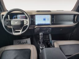 Interior view of a 2022 Ford Bronco Wildtrak Sasquatch showcasing the dashboard, steering wheel, and dual display screens, highlighting modern design and technology features.