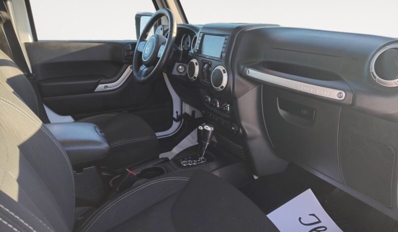 Interior view of a 2018 Jeep Wrangler Unlimited Sahara, featuring black seating, dashboard controls, and a touchscreen display, emphasizing its modern design and adventure-ready capabilities.