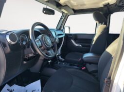 Interior view of a 2018 Jeep Wrangler Sahara Unlimited, showcasing black fabric seats, steering wheel, and dashboard features, emphasizing the vehicle's adventure-ready design and comfort.