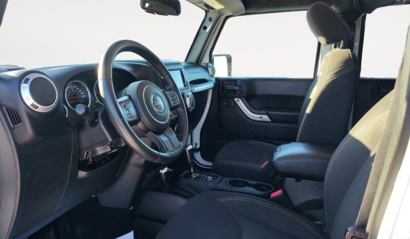 Interior view of a 2018 Jeep Wrangler Sahara Unlimited 4&times;4 showcasing black fabric seats, steering wheel with controls, dashboard with gauges, and gear shift, emphasizing adventure-ready features.