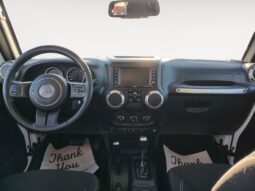 Interior view of a 2018 Jeep Wrangler Unlimited Sahara, featuring a steering wheel, dashboard with infotainment system, and gear shifter, showcasing black upholstery and "Thank You" mats on the floor.