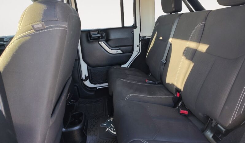 Interior view of the rear seating area of a 2018 Jeep Wrangler Unlimited Sahara, featuring black fabric seats, door panel details, and floor mats, highlighting spaciousness for passengers.