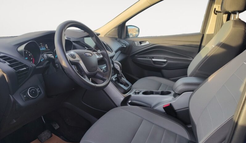 Interior view of a 2015 Ford Escape SE showcasing gray seating, dashboard with Ford branding, and controls, highlighting comfort and utility for potential buyers.