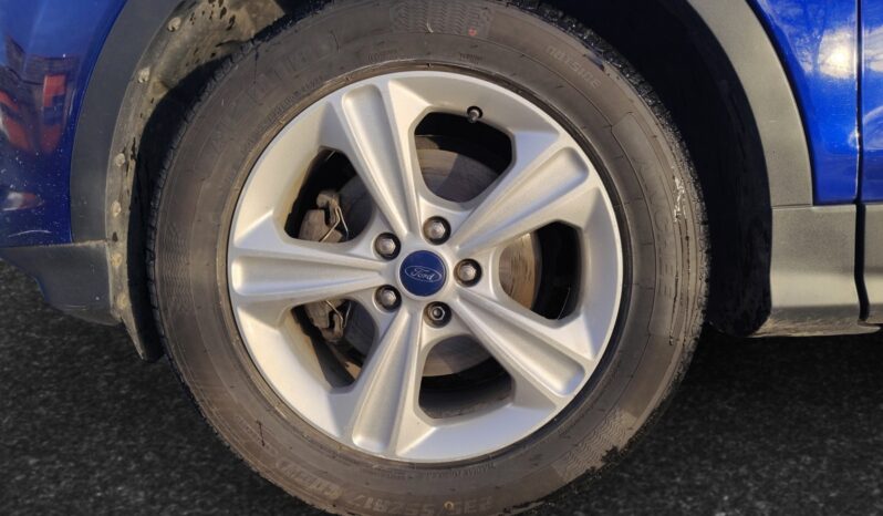 Close-up of a silver alloy wheel with a Ford logo, mounted on a blue 2015 Ford Escape SE, showcasing its sporty design and tire tread.